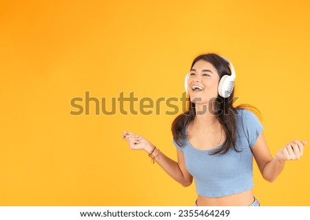 Studio photo with yellow background of an hispanic young woman singing and listening to music using headphones