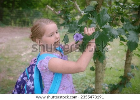 First grader picking a flower from a tree. 1st grader with back pack. Student picking flower. Royalty-Free Stock Photo #2355473191