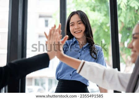 A beautiful and cheerful Asian businesswoman is putting her hand up or giving high fives to her team during the meeting. Teamwork, team building, support, together, celebrating success Royalty-Free Stock Photo #2355491585