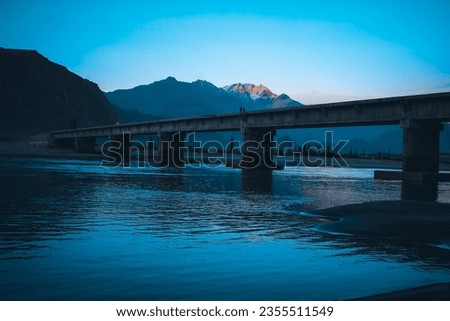 bridge over the river and water running under the bridge snow covered mountain and blue sky in a background 