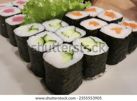 a photography of a plate of sushi rolls with lettuce and cucumber, plate of sushi rolls with cucumber and lettuce on top.