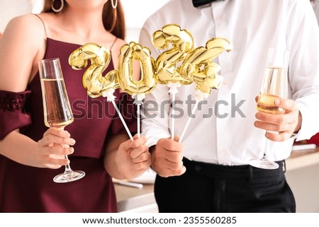 Young couple with champagne and figure 2024 celebrating Christmas in kitchen, closeup