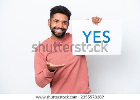 Young Brazilian man isolated on white background holding a placard with text YES making a deal