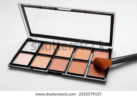 Colorful contouring palette with brush on light grey background, closeup. Professional cosmetic product