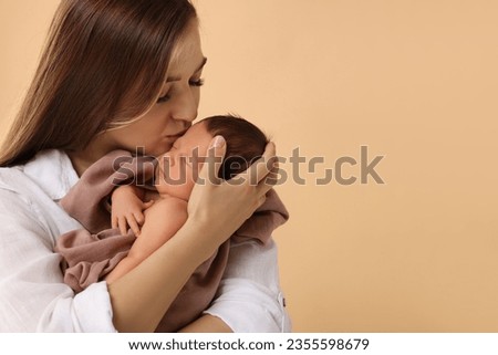 Mother kissing her cute newborn baby on beige background. Space for text
