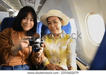 Happy senior woman and daughter sitting in passenger airplane and taking picture, waiting for airplane landing