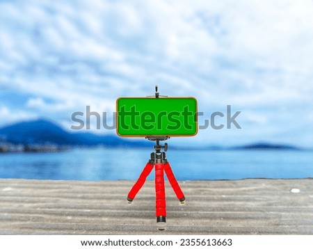 Smartphone with green screen mounted on a tripod on nature, sea, and sky  background, mockup for design