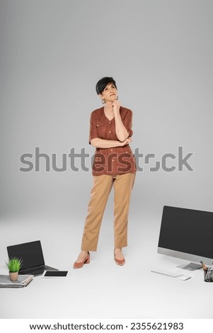 thoughtful mature businessman in trendy autumn clothes near digital devices and documents on grey