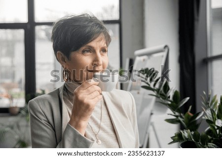 successful middle aged woman, corporate manager, drinking coffee and looking away in office
