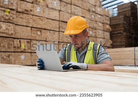Male warehouse worker wearing uniform working with labtop computer in wooden warehouse storage