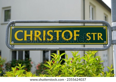 German street sign: Christof Straße. Green sign with yellow print. Large letters. Sign at the street in front of a garden. Sign for name of the street