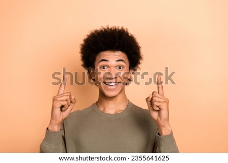 Photo of positive impressed guy with afro hairdo wear khaki shirt impressed directing empty space isolated on beige color background