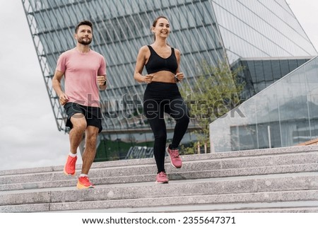 A running instructor and a client are training fitness outdoors. A woman and a man are friends in fitness clothes for sports. People use fitness watches and running shoes.