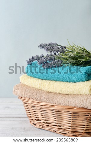  Stack of bath towels with lavender flowers in a wicker basket on light wooden background 