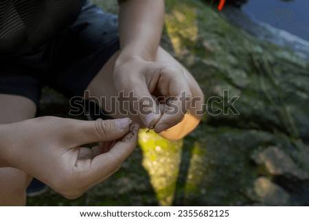 The hands of a teenager trying to put worms on a hook for fishing. Sport fishing on the river in summer.