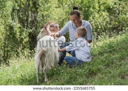 woman and a children keep a goat in the pasture