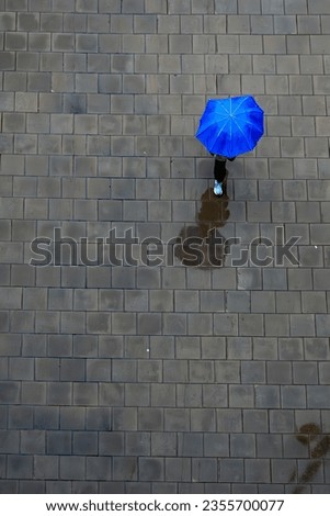Stockholm, Sweden An unidentified person walks  on the sidewalk in the rain with a blue umbrella. Royalty-Free Stock Photo #2355700077