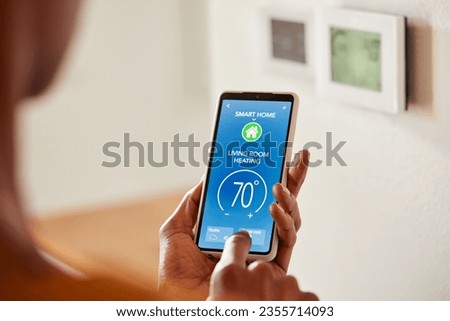 Close up of black female hand setting temperature of air conditioner or heat pump using smartphone at home. Back view of african american woman use smart home. Energy efficiency, savings and ecology.