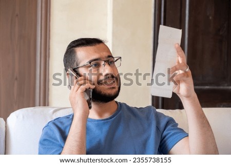 young bearded man making call while holding receipts
