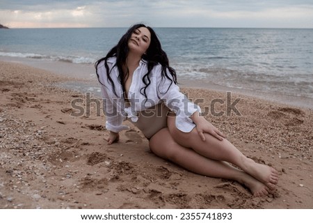 beautiful plus size woman with long haiws walking in the beach against the sea.. The overweight model wearing style shirt and and bikini