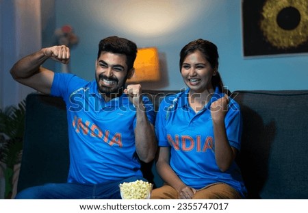 Indian couples celebrating indias win while watching live cricket sports match on tv or television at home - concept of Victory Celebration, Excited Fans and Emotional moment Royalty-Free Stock Photo #2355747017