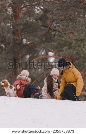 Three adorable young girls having fun together by beautiful frozen park, forest. Cute sisters playing in a snow with a dog. The concept of Christmas and New Year