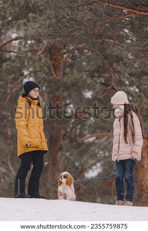 Two adorable young girls having fun together by beautiful frozen park, forest. Cute sisters playing in a snow with a dog. The concept of Christmas and New Year
