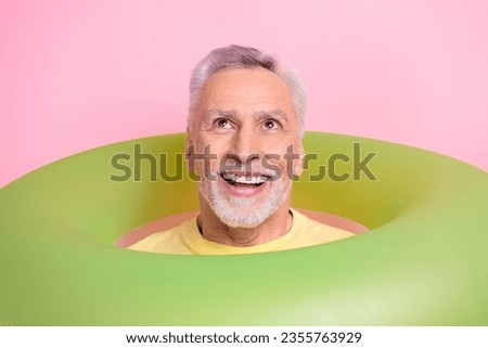 Portrait of impressed funny person with white hair swim in inflatable ring look up at empty space isolated on pink color background