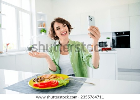 Photo of excited shiny young girl wear green shirt eating breakfast recording video modern gadget indoors kitchen room