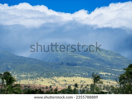 The West Maui Mountains sit still as clouds roll in from the coast and palm tress bend in high winds