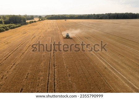 Drone photography of farmer with a combine harvesting a yellow agriculture grain field during summer sunny day.