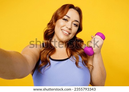 Close up young plus size big fat fit woman wear blue top warm up train do selfie shot pov on mobile cell phone hold muscles isolated on plain yellow background studio home gym. Workout sport concept