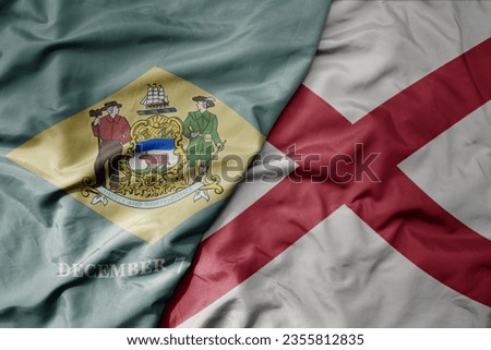 big waving colorful national flag of alabama state and flag of delaware state . macro