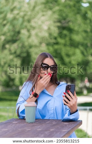 Summer portrait of a girl with long blond hair. A girl in a blue shirt and sunglasses holds a smartphone in her hands and talks on a video call. High quality photo