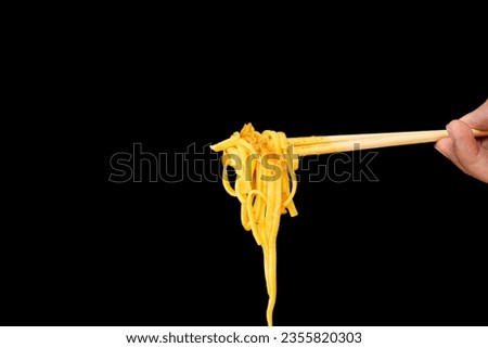 The hand that uses chopsticks to pick up the rice noodles on black background. Khao soi, Northern style curried noodle soup. Thai food style