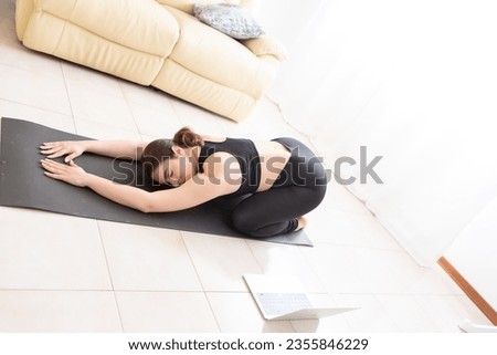 Young woman doing yoga and gymnastics in streaming with a laptop in her apartment to regain fitness after pregnancy