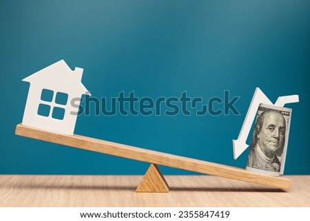 Buying cheap real estate. Banner on the theme of buying a house. One hundred dollar bill with an arrow pointing down and a house model on the scales as a symbol of a good real estate deal.