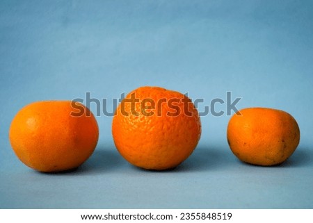 Three oranges of different sizes and shapes on a blue background, can be used for a magazine cover