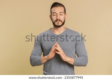 Keep calm down, relax, inner balance. Young lebanese man breathes deeply with mudra gesture, eyes closed, meditating with concentrated thoughts, peaceful mind. Middle eastern guy on beige background