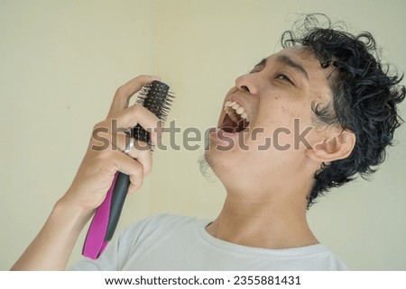 Young curly man wear white t-shirts when singing gesture with comb. The photo is suitable to use for expression and gesture content media.