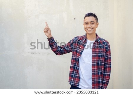 Indonesian man wear casual clothes with click thumbnail pose. The photo is suitable to use for man expression advertising and fashion life style. Royalty-Free Stock Photo #2355883121