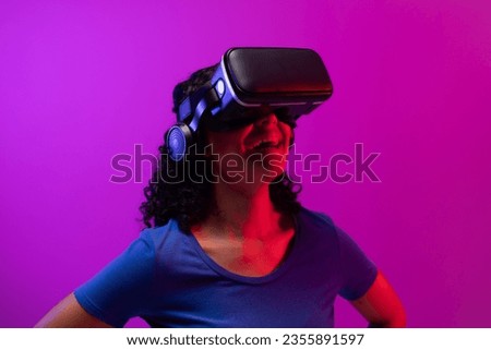 Biracial woman using vr headset on neon pink to purple background. Technology, digital networks, global connections and communication metaverse.