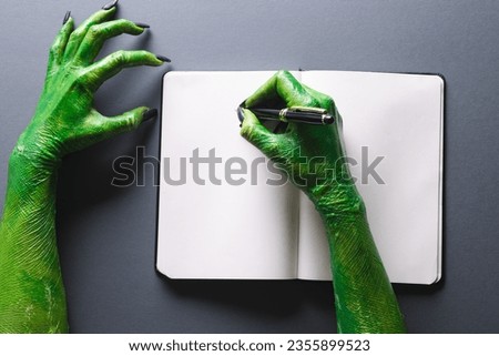 Green monster hands writing notebook with copy space on grey background. Halloween, tradition and celebration concept.
