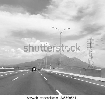 a black and white photo depicting a freeway transportation route with beautiful backdrop of mountain and sky views