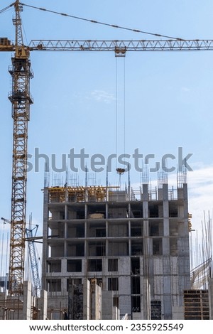 A crane and a building under construction against a blue sky background. Builders work on large construction sites, and there are many cranes working in the field of new construction.