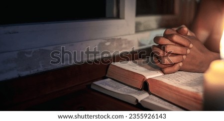 Hands praying on holy bible in the light candles at window background, Religion concept.