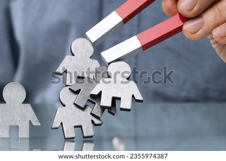 Close-up Of A Human Hand Attracting Red Human Figures With Horseshoe Magnet On White Background Royalty-Free Stock Photo #2355974387