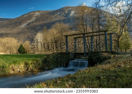 Small waterfall under a bridge and mountains