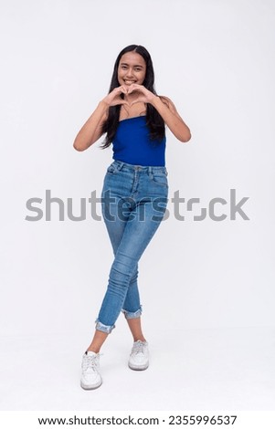 A young pretty asian woman making a heart shape with both hands. Full body photo isolated on a white background.