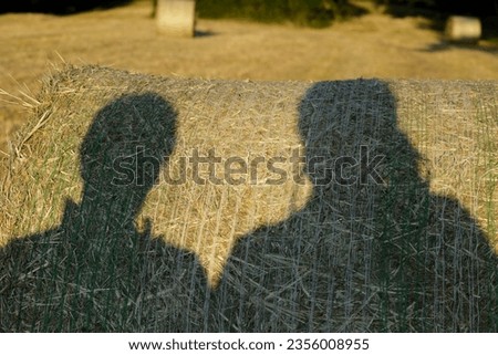 2 people cast a shadow on a hay bale